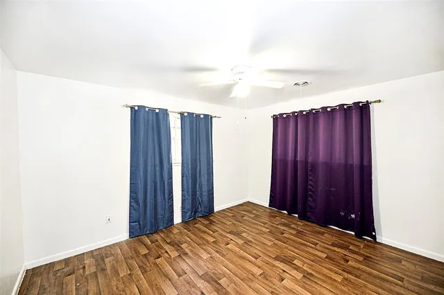 an empty room with wooden floor chandelier fan and windows