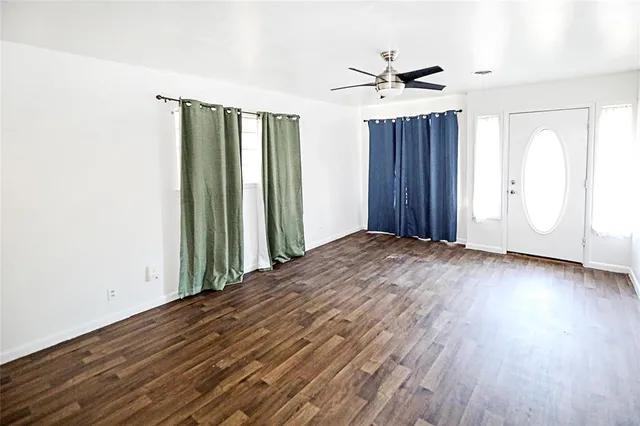 an empty room with wooden floor windows and fan