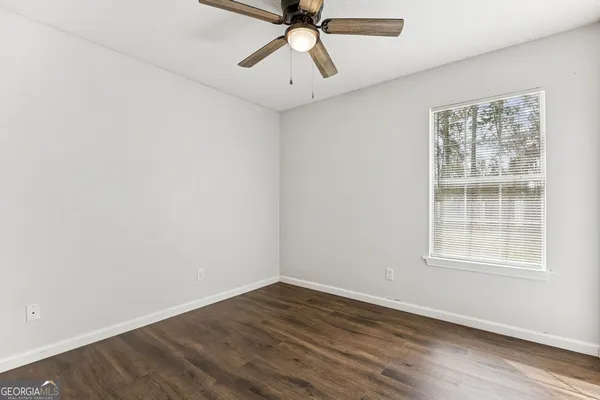 an empty room with wooden floor ceiling fan and windows