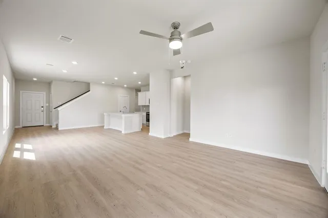 a view of an empty room with wooden floor and a ceiling fan