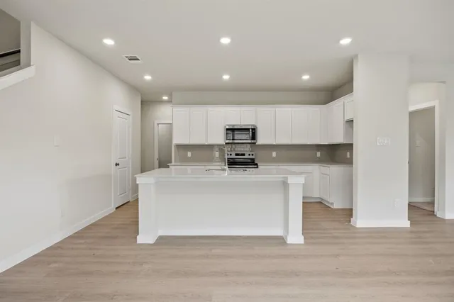 a view of kitchen with stainless steel appliances granite countertop refrigerator oven a sink and white cabinets