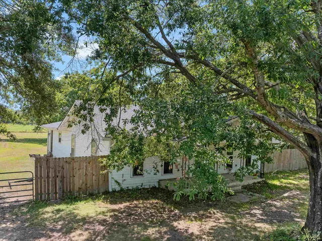 a view of a yard in front of a house with large trees and wooden fence