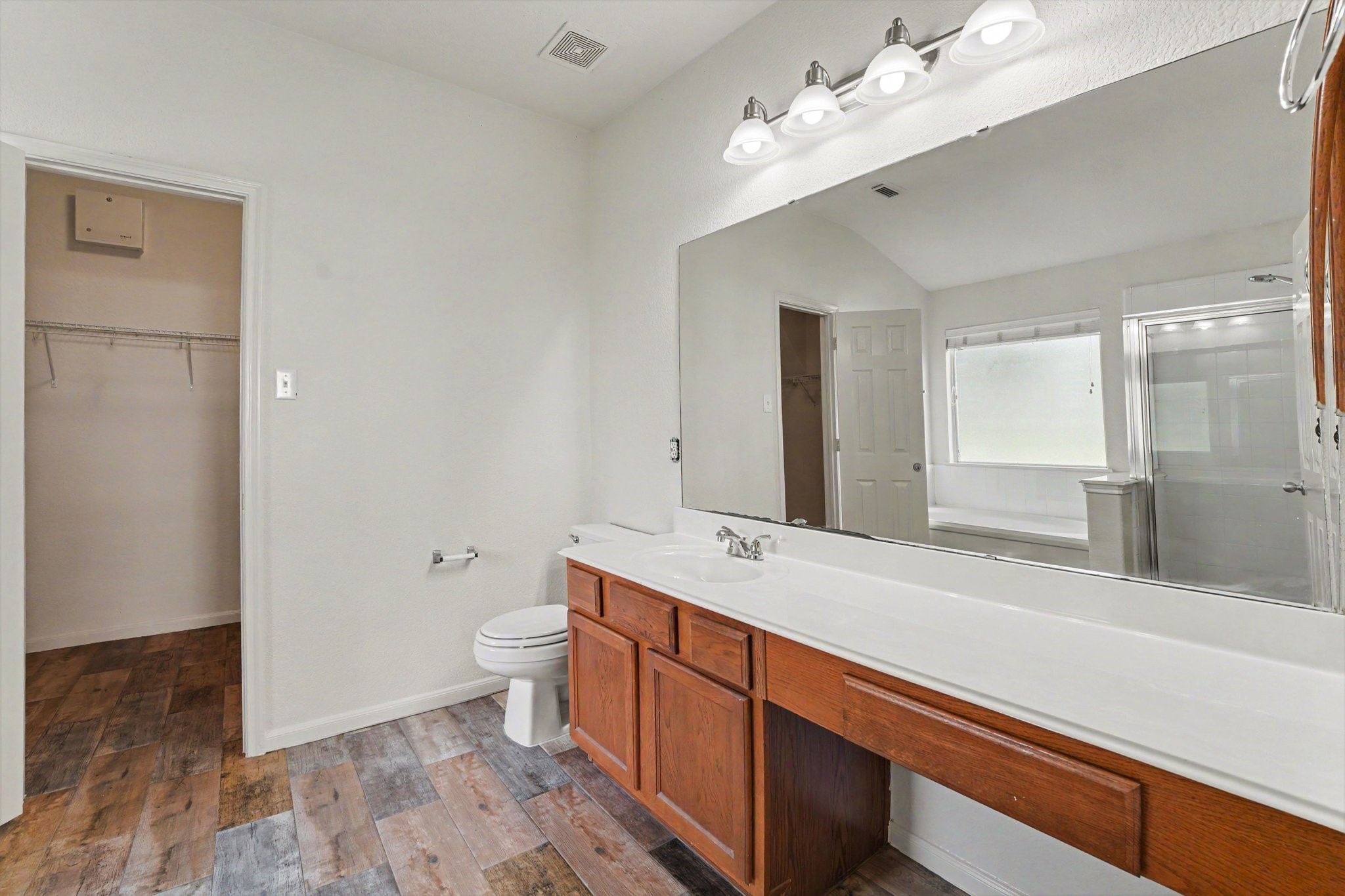 21427 Blooming Rock Lane Spring, TX 77379 - Photo 19 of 32 This bathroom features a large mirror with a wooden vanity, ample countertop space, and a four-light fixture. It has a walk-in closet, wood-look tile flooring, and a glass-enclosed shower. The room is bright and spacious, ideal for comfortable daily use.