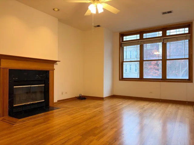a view of an empty room with wooden floor fireplace and a window