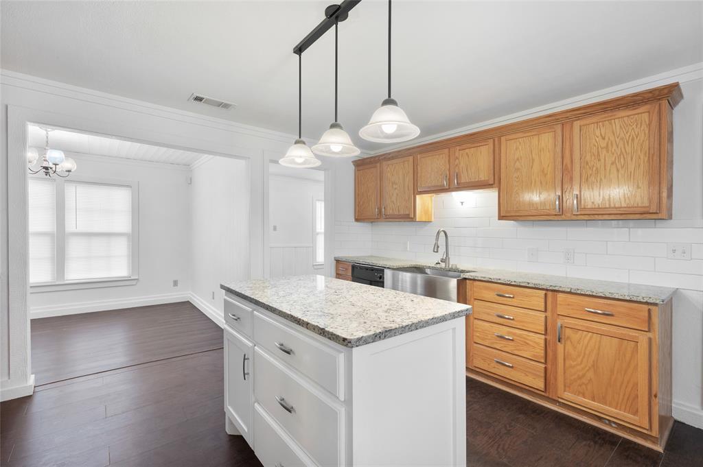 903 Lynn Street Bonham, TX 75418 - Photo 11 of 29 a kitchen with granite countertop cabinets a sink dishwasher a stove and a dining table with wooden floor
