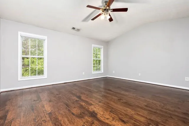 an empty room with wooden floor fan and windows