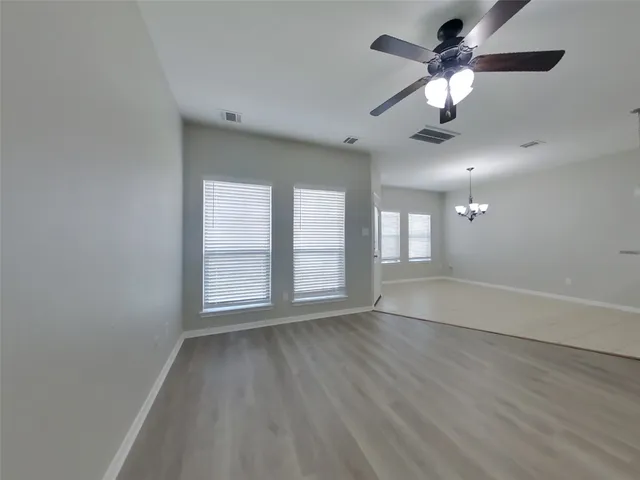 an empty room with wooden floor chandelier fan and windows