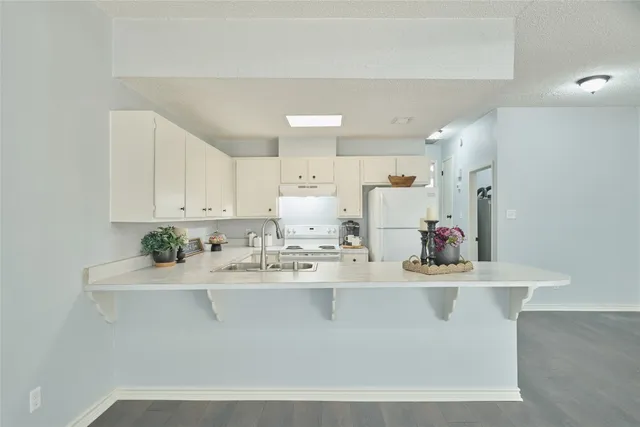 a room with kitchen island a sink a stove and white cabinets