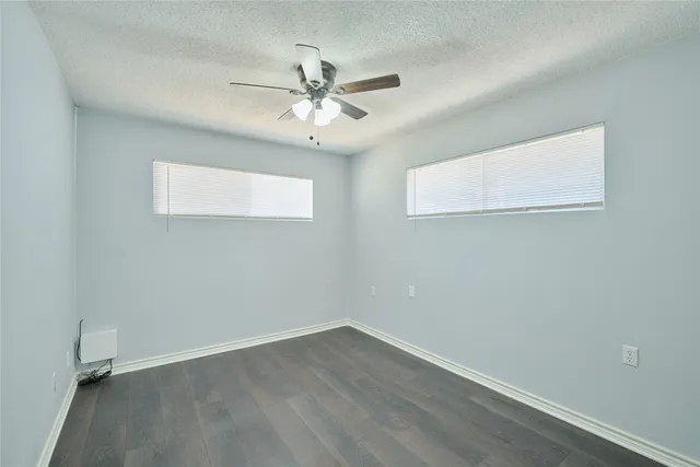 an empty room with wooden floor fan and windows