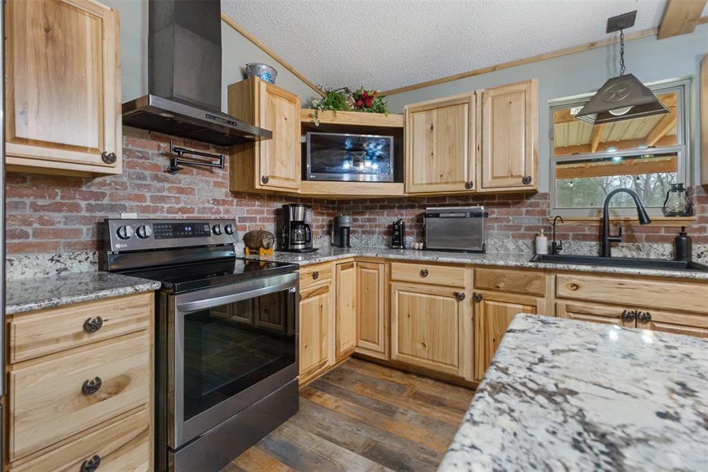 7766 North State Highway 78 Ravenna, TX 75476 - Photo 7 of 39 Kitchen featuring light brown cabinetry, appliances with stainless steel finishes, wall chimney range hood, light stone countertops, and a textured ceiling