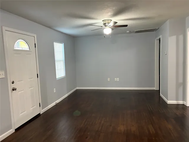 an empty room with wooden floor chandelier fan and windows