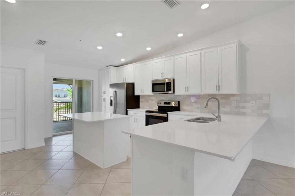 6047 Ellerston Way, Unit 2125 Ave Maria, FL 34142 - Photo 4 of 41 Kitchen with stainless steel appliances, island, tiled backsplash, quartz countertops