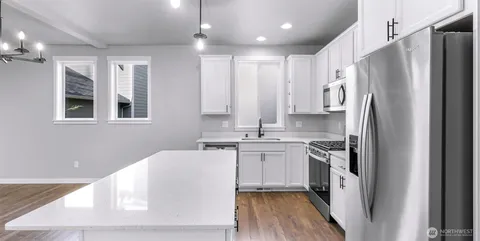 a large kitchen with stainless steel appliances kitchen island a sink dishwasher a refrigerator and white cabinets with wooden floor