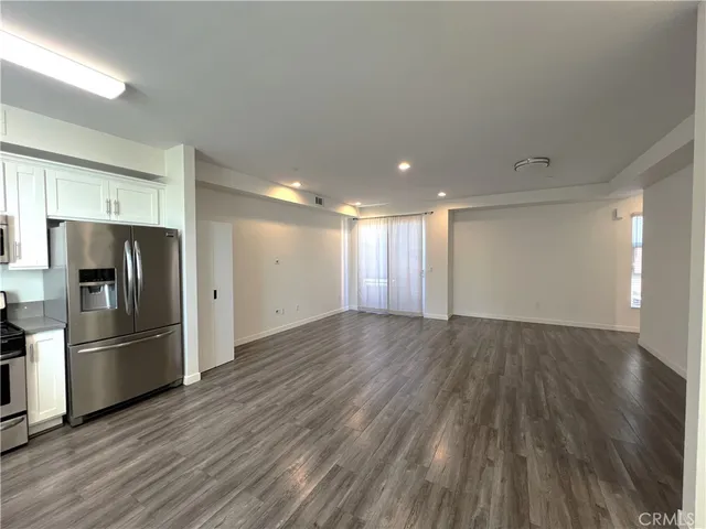 a view of an empty room with wooden floor and a kitchen