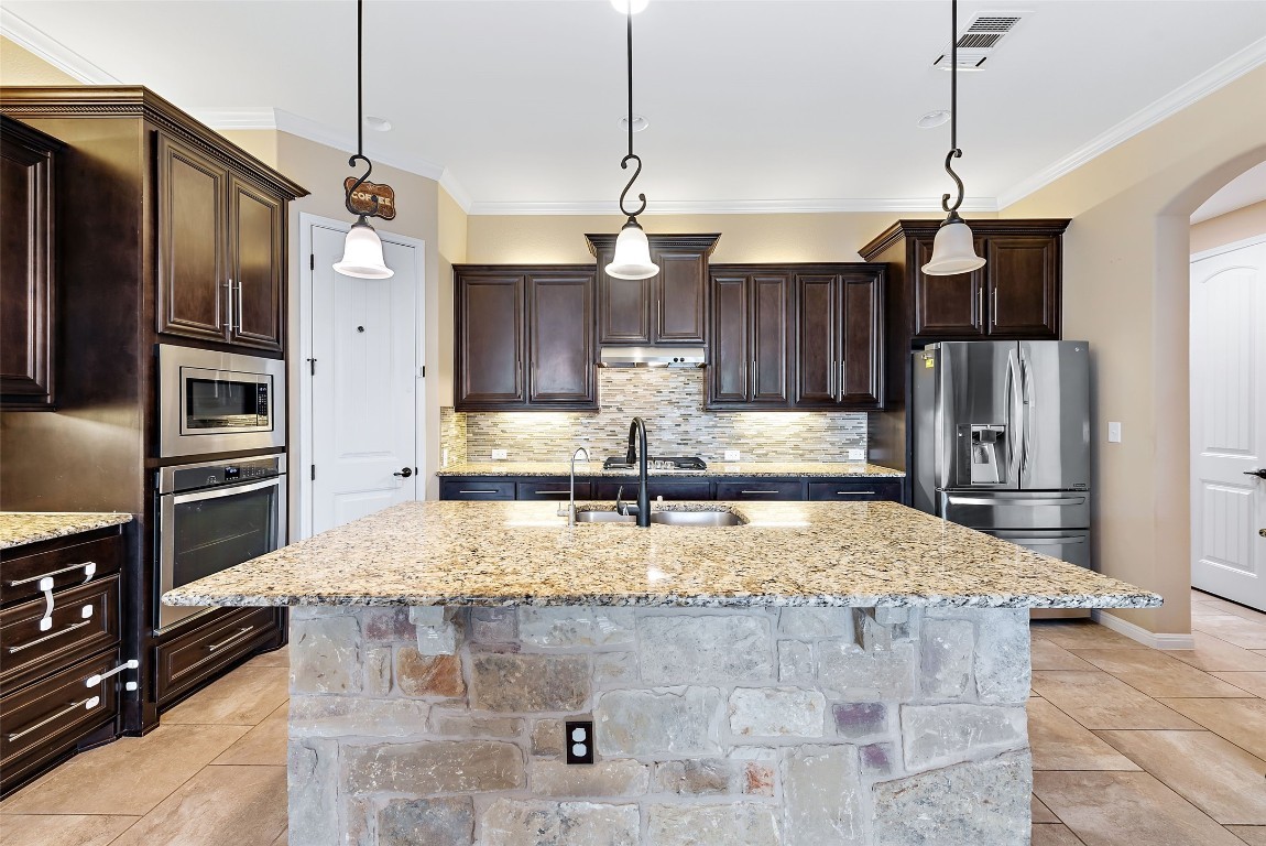 2000 Manada Trail Leander, TX 78641 - Photo 13 of 36 A well-appointed kitchen features a large stone-clad island, rich wood cabinetry, and integrated stainless steel appliances.