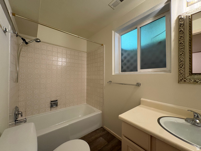 595 Meadowlark Road Orem, UT 84097 - Photo 60 of 87 Bathroom featuring a white bathtub with patterned tile surround, a built-in vanity with integrated sink, and wood-finish flooring