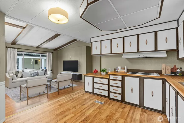 a living room with stainless steel appliances granite countertop a stove a sink dishwasher and white cabinets with wooden floor