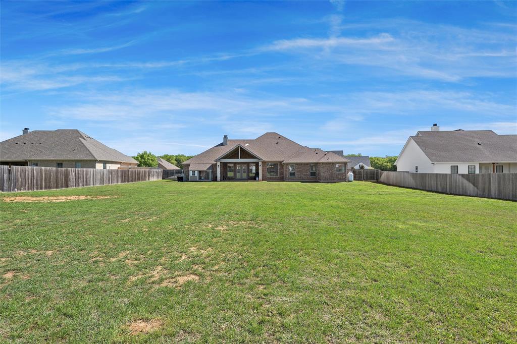 23 Independence Trail Waco, TX 76708 - Photo 30 of 35 Expansive backyard featuring a large green lawn, full wood-plank fencing, and a covered patio area with a vaulted ceiling