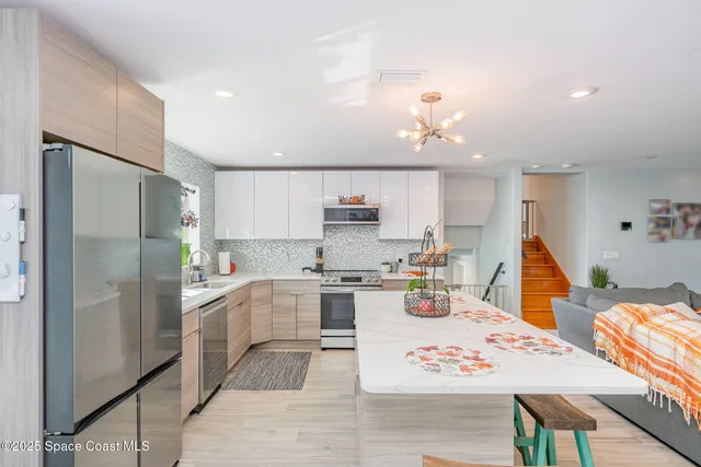 a kitchen with stainless steel appliances kitchen island granite countertop a refrigerator oven a sink a dining table and chairs with wooden floor