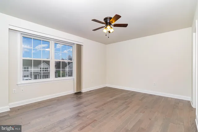 a view of an empty room with window a ceiling fan and wooden floor