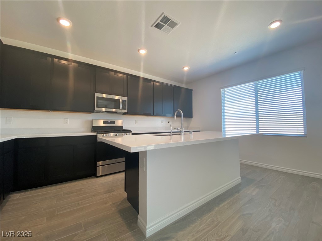 8846 Sasquatch Run Avenue Las Vegas, NV 89166 - Photo 6 of 21 Kitchen featuring dark cabinets, stainless steel appliances, light wood-style floors, a kitchen island with sink, and recessed lighting