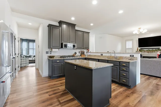 a kitchen with stainless steel appliances granite countertop a stove top oven a sink dishwasher and a refrigerator with wooden floor