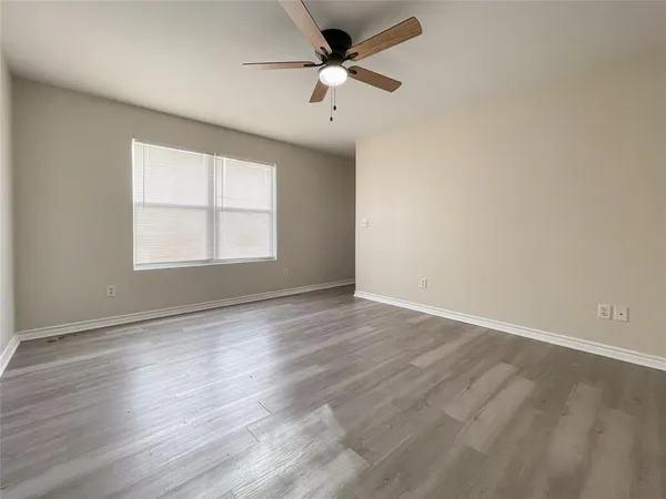 an empty room with wooden floor ceiling fan and windows