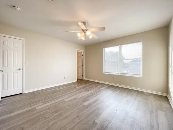 an empty room with wooden floor chandelier fan and windows