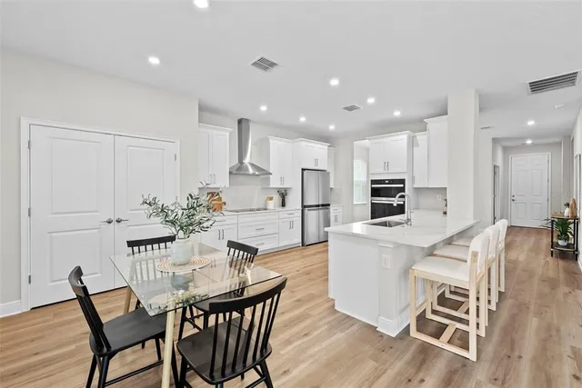 a kitchen with stainless steel appliances kitchen island granite countertop a dining table chairs and white cabinets