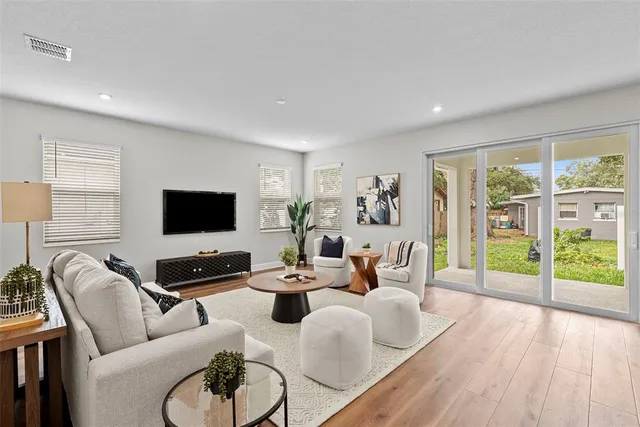 a living room with furniture floor to ceiling window hardwood floor and a flat screen tv