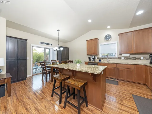 a dining hall with stainless steel appliances granite countertop a stove a refrigerator a kitchen island a dining table and chairs with wooden floor