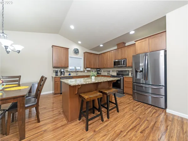 a kitchen with stainless steel appliances a refrigerator a stove a dining table and chairs with wooden floor