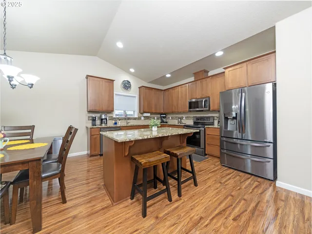 a kitchen with stainless steel appliances a refrigerator a stove a dining table and chairs with wooden floor