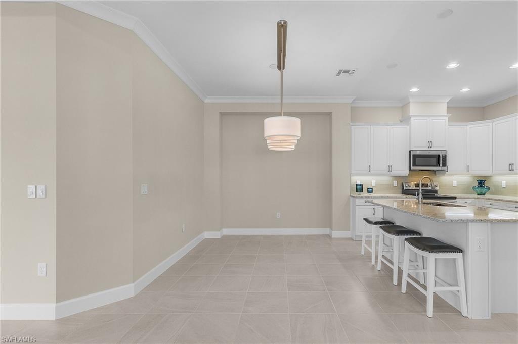 5731 Highbourne Drive Naples, FL 34113 - Photo 4 of 20 Kitchen featuring appliances with stainless steel finishes, light stone counters, sink, decorative light fixtures, and white cabinets
