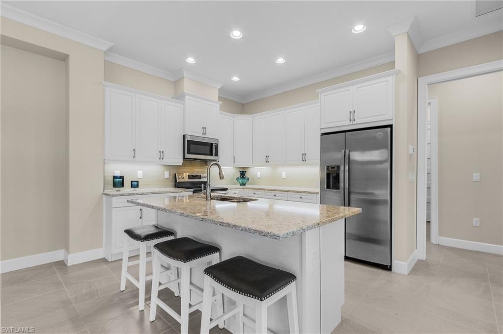 5731 Highbourne Drive Naples, FL 34113 - Photo 5 of 20 Kitchen featuring a kitchen island with sink, sink, appliances with stainless steel finishes, tasteful backsplash, and white cabinetry