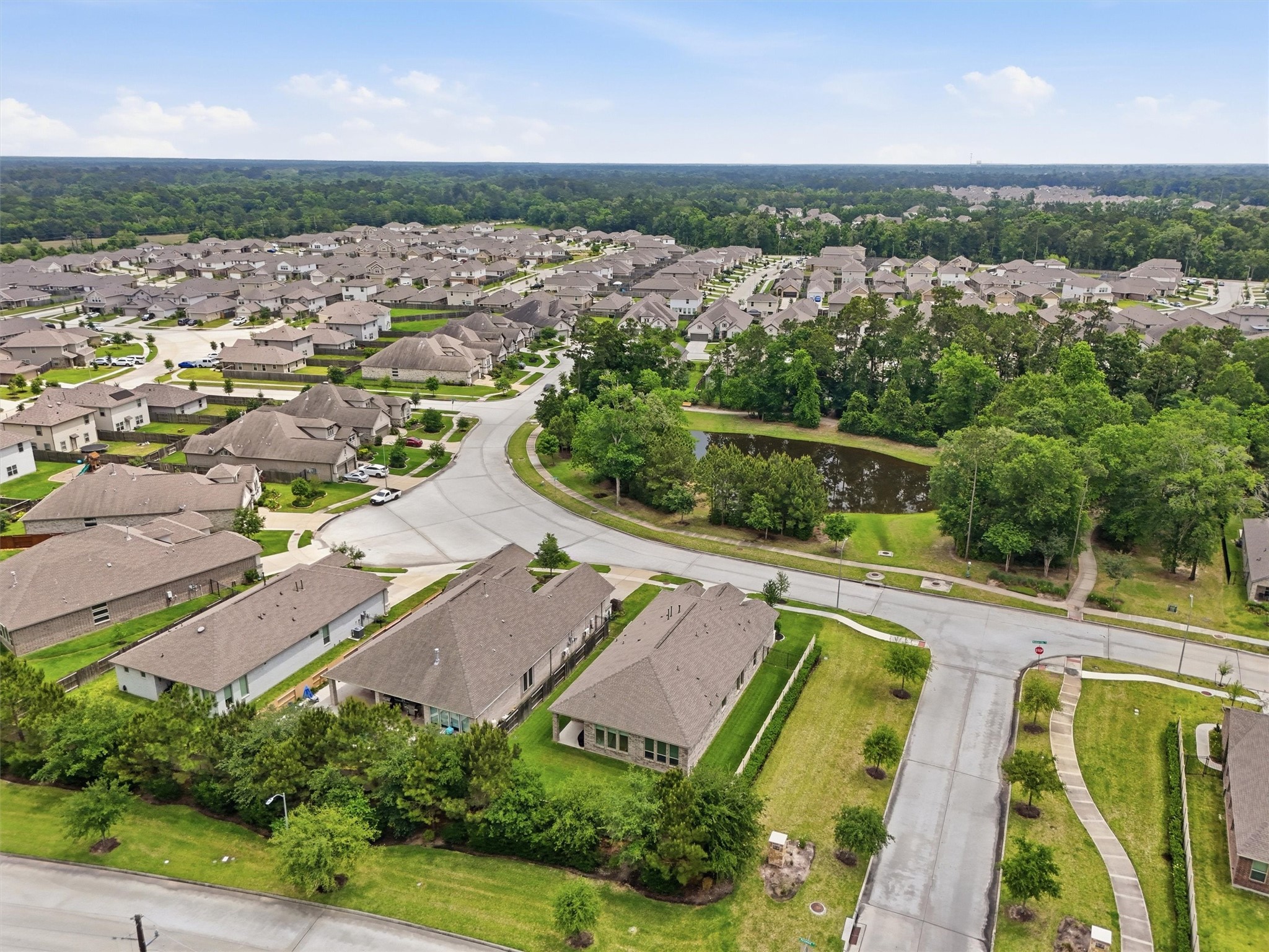 6071 Windward Falls Way Porter, TX 77365 - Photo 31 of 33 This aerial photo showcases a suburban neighborhood with well-maintained homes, spacious yards, and tree-lined streets. A small pond adds a natural touch, and nearby greenery provides a serene environment. The area appears peaceful and ideal for families.
