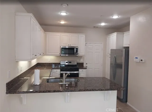 a kitchen with kitchen island granite countertop a sink a stove a refrigerator and white cabinets