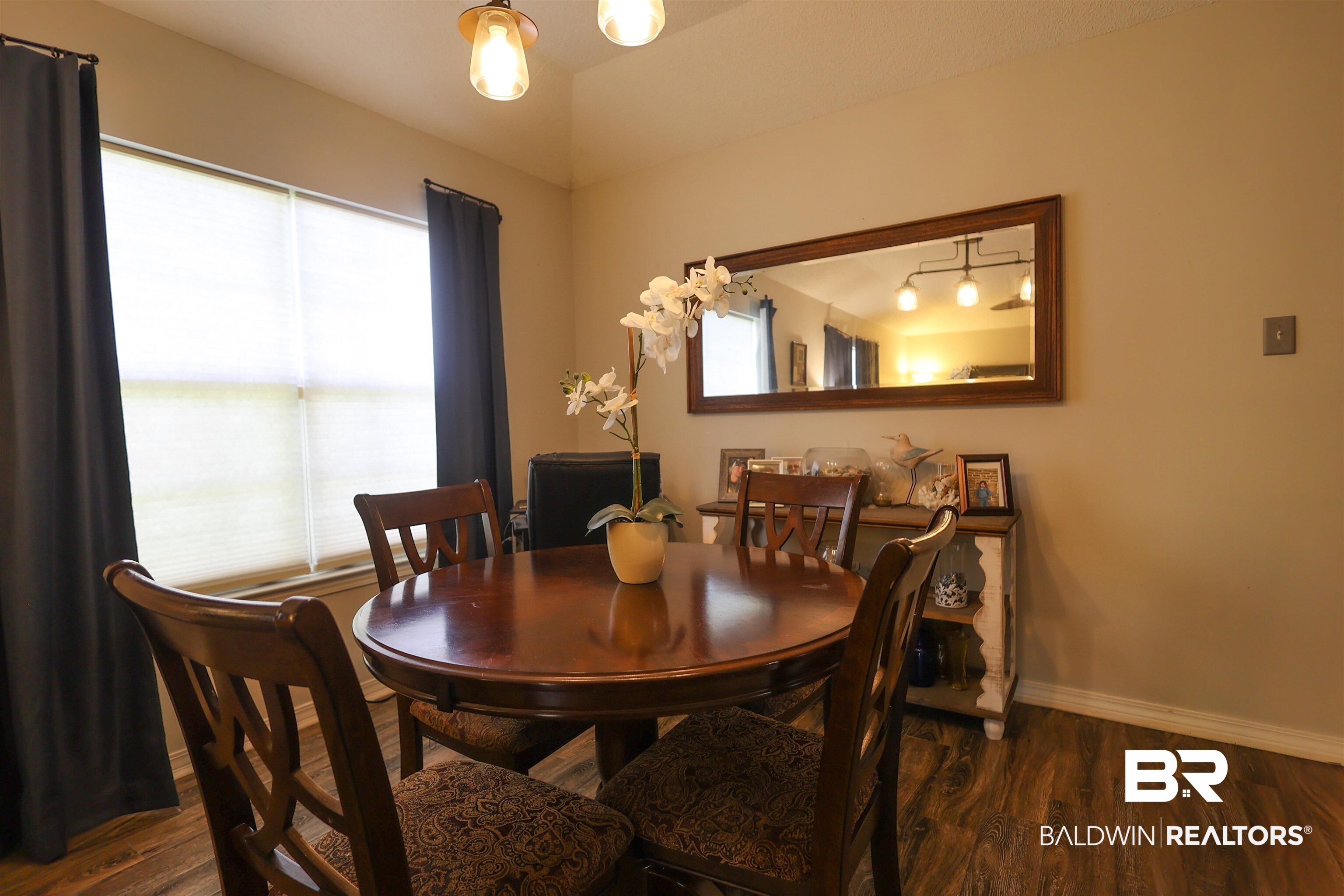7790 Audubon Drive Foley, AL 36535 - Photo 13 of 39 Dining area featuring wood-finish flooring, a large window with privacy blinds, and a decorative wall mirror with a wood frame