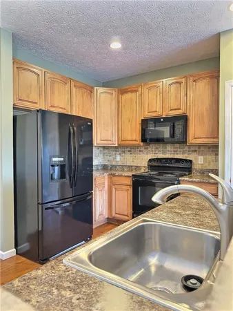 a kitchen with granite countertop a stove a sink dishwasher a refrigerator and wooden cabinets