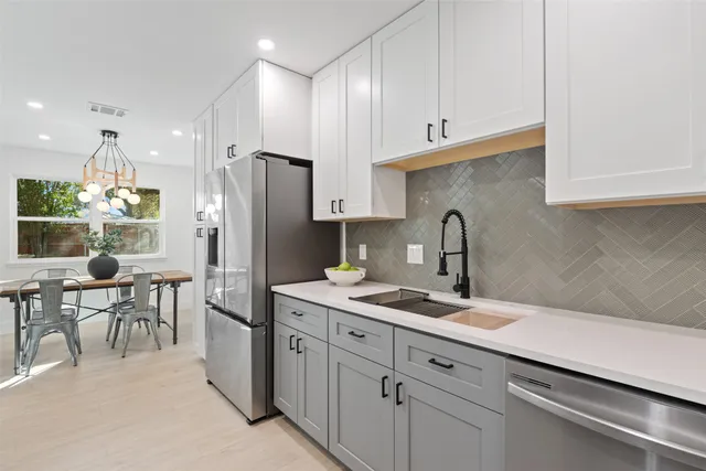 a kitchen with stainless steel appliances a sink a stove a refrigerator cabinets and a dining table