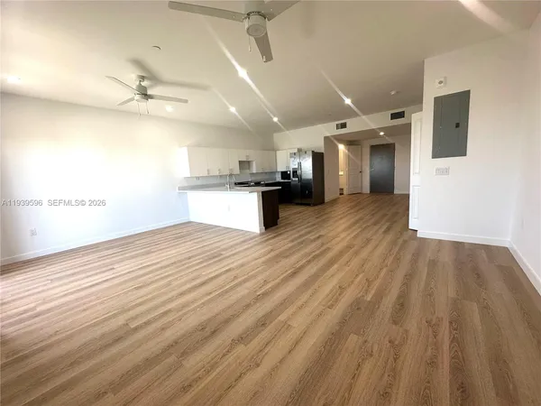 an empty room with kitchen view and wooden floor