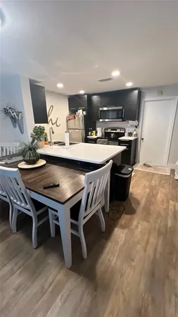 a dining hall with stainless steel appliances a dining table wooden floor and a rug