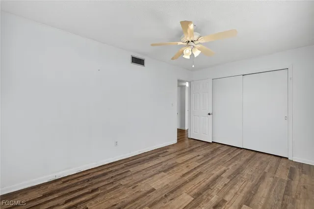 a view of an empty room with wooden floor and a ceiling fan