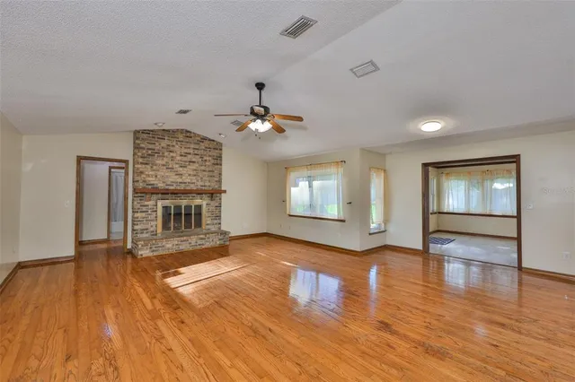a view of an empty room with wooden floor fireplace and a window