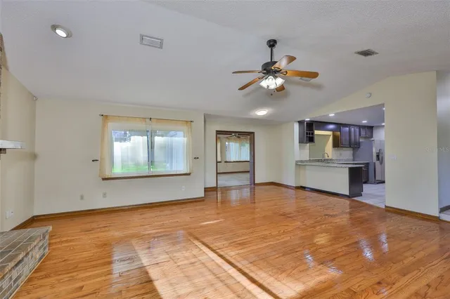 a view of an empty room with kitchen and window