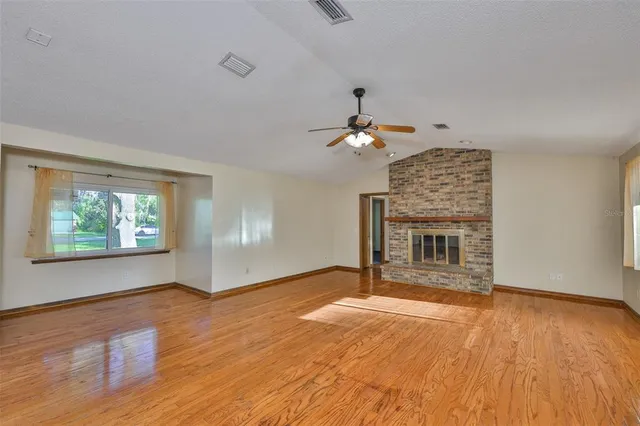 a view of an empty room with wooden floor fireplace and a window