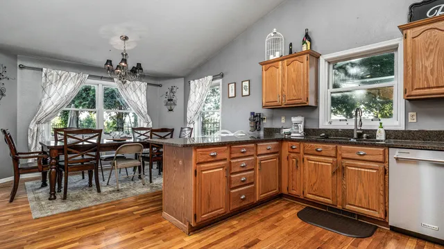 a open kitchen with stainless steel appliances granite countertop a stove top oven a sink dishwasher a dining table and chairs with wooden floor