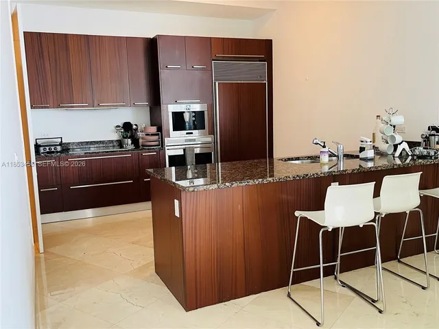 a kitchen with stainless steel appliances kitchen island granite countertop a table chairs and a refrigerator