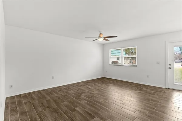 an empty room with wooden floor chandelier fan and windows