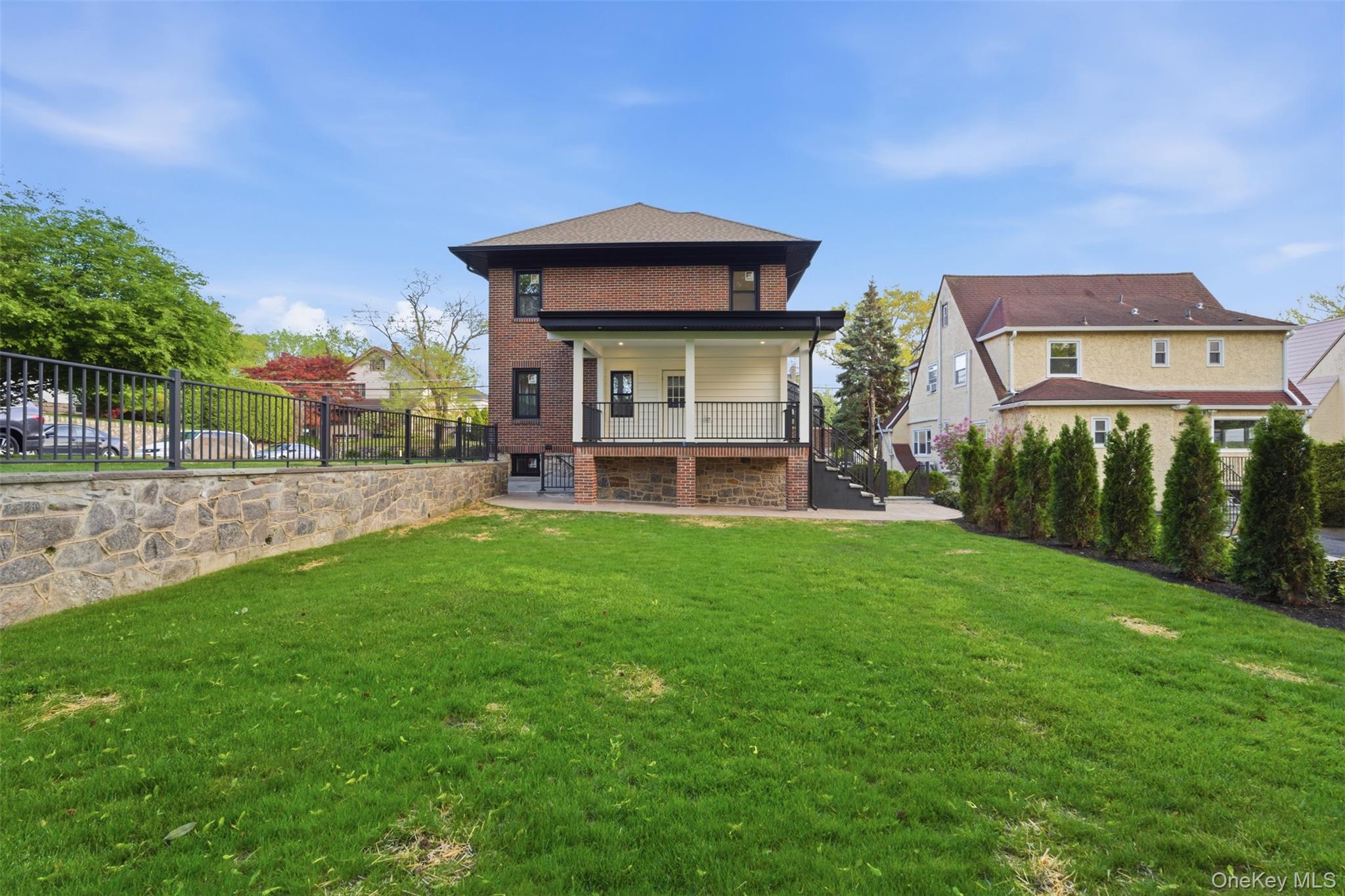 40 Calhoun Avenue New Rochelle, NY 10801 - Photo 40 of 49 Expansive rear yard featuring a manicured lawn, a stone retaining wall with black metal fencing, and a covered porch with black railings